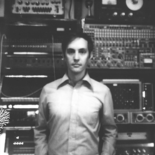 Black and white photo of Beau in front of a wall of recording equipment